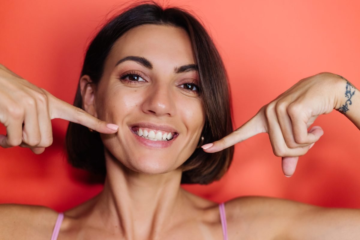 Close portrait of woman on red background shows point fingers on white teeth smile